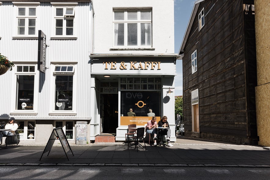 Street view of Te & Kaffi café on Laugavegur in Reykjavik, Iceland, with customers enjoying coffee at outdoor tables in front of the white historic building.
