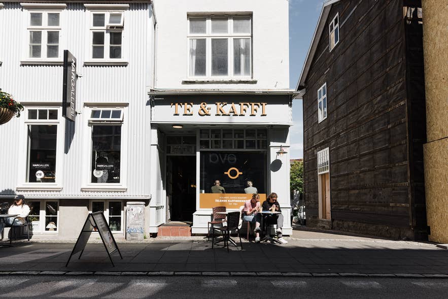 Street view of Te & Kaffi café on Laugavegur in Reykjavik, Iceland, with customers enjoying coffee at outdoor tables in front of the white historic building. Street view of Te & Kaffi café on Laugavegur in Reykjavik, Iceland, with customers enjoying coffee at outdoor tables in front of the white historic building.