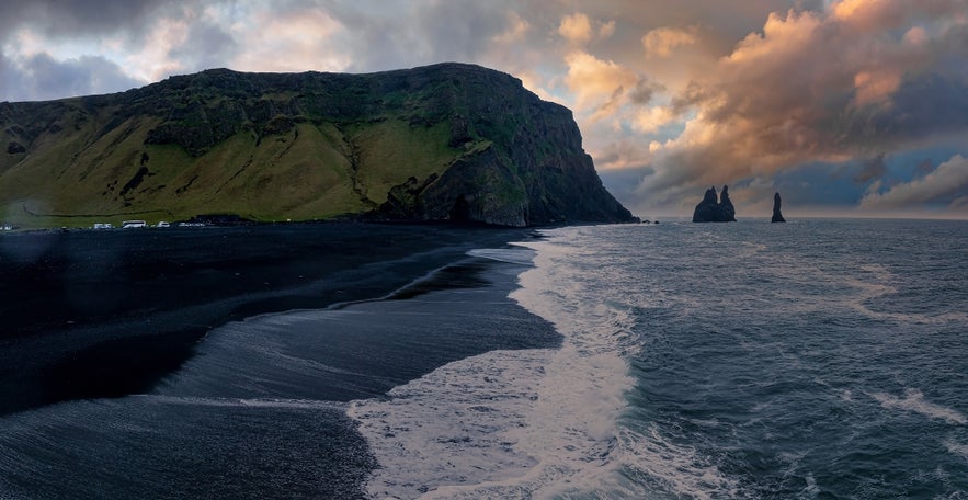 Reynisfjara Beach with black sands, cliffs, and sea stacks at sunset