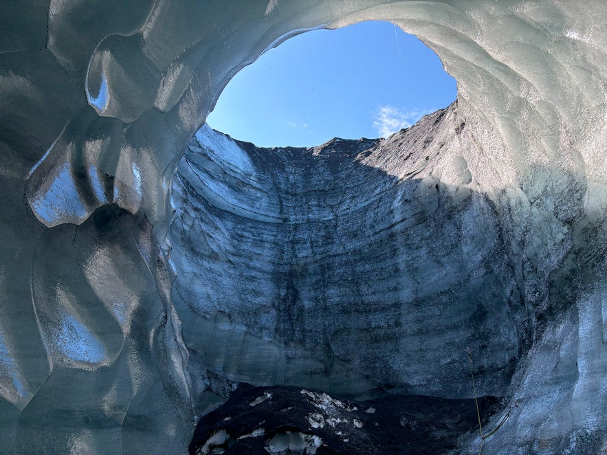 View from inside a glistening glacier cave, looking up at the sky