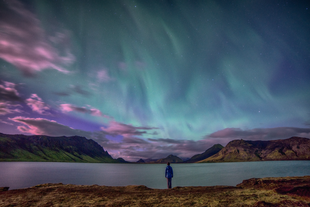 A man stands in the beautiful Icelandic nature admiring the northern lights.