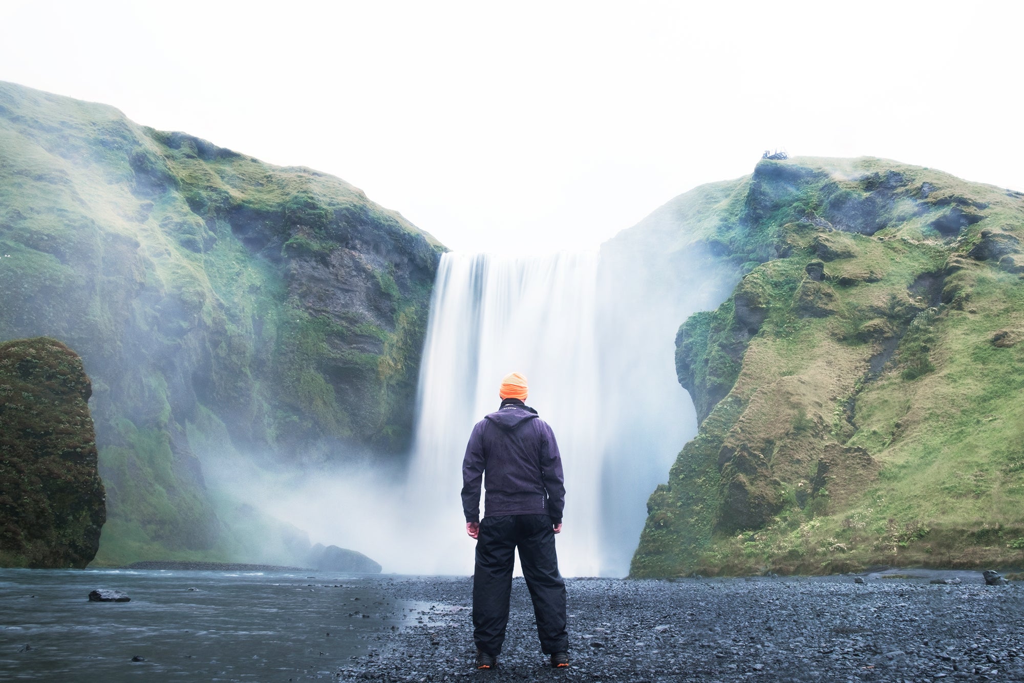 A traveler takes a photo in front of the Skogafoss waterfall.