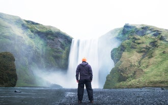 A traveler takes a photo in front of the Skogafoss waterfall.