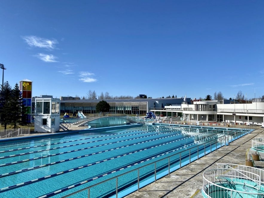 Outdoor swimming pools and slides at Laugardalslaug Pool Complex in Reykjavik in April under a clear blue sky.