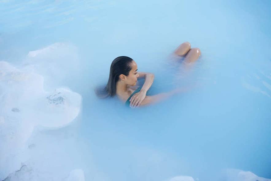 Jeune femme se baignant dans les eaux géothermiques bleu laiteux du Blue Lagoon en Islande, profitant d’une expérience spa apaisante