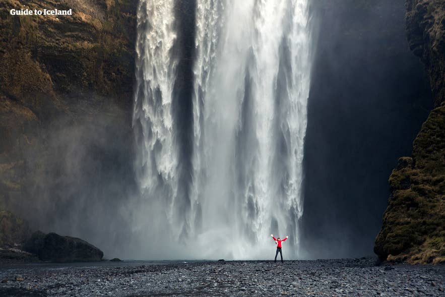 Podróżny stojący przed wodospadem Skogafoss na południowym wybrzeżu Islandii — popularny przystanek podczas jednodniowych wycieczek z przewodnikiem z Reykjaviku bez samochodu.