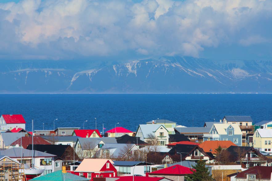 Kleurrijke daken in Keflavik, IJsland, met de berg Esja en de baai Faxafloi op de achtergrond onder een helderblauwe hemel met indrukwekkende wolken.