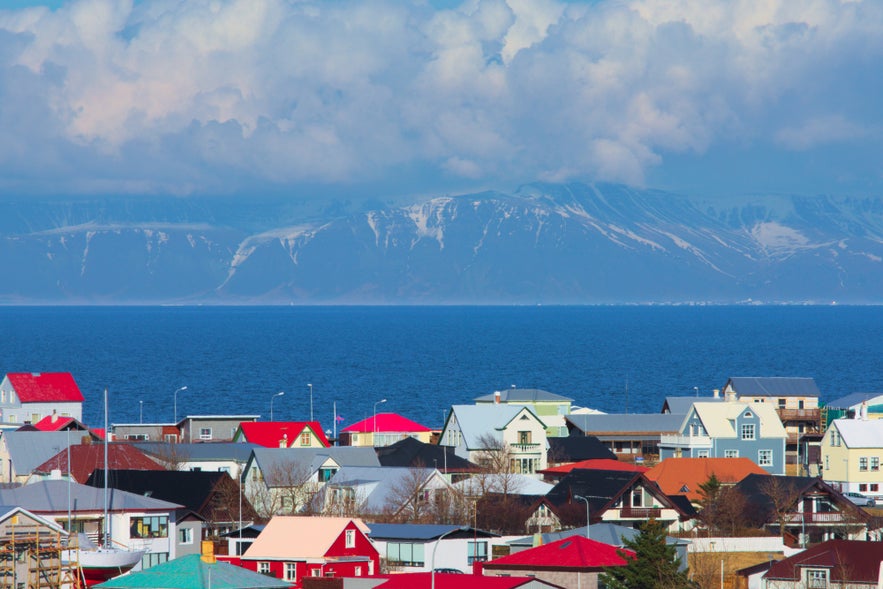 Bunte Hausd&auml;cher in Keflavik in Island, mit dem Berg Esja und der Faxafloi-Bucht im Hintergrund &ndash; unter einem leuchtend blauen Himmel mit dramatischen Wolken.
