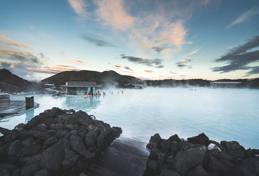 Mensen die bij zonsondergang ontspannen in de geothermische spa Blue Lagoon in IJsland, omringd door stoom en vulkanische lavastenen, met schilderachtig uitzicht op de bergen.