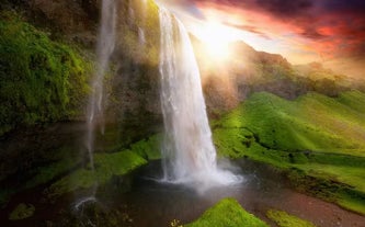 The sun shining over Seljalandsfoss waterfall on Iceland's South Coast.