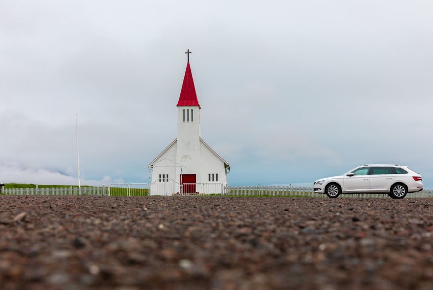 A car parked in front of a small church in Iceland.