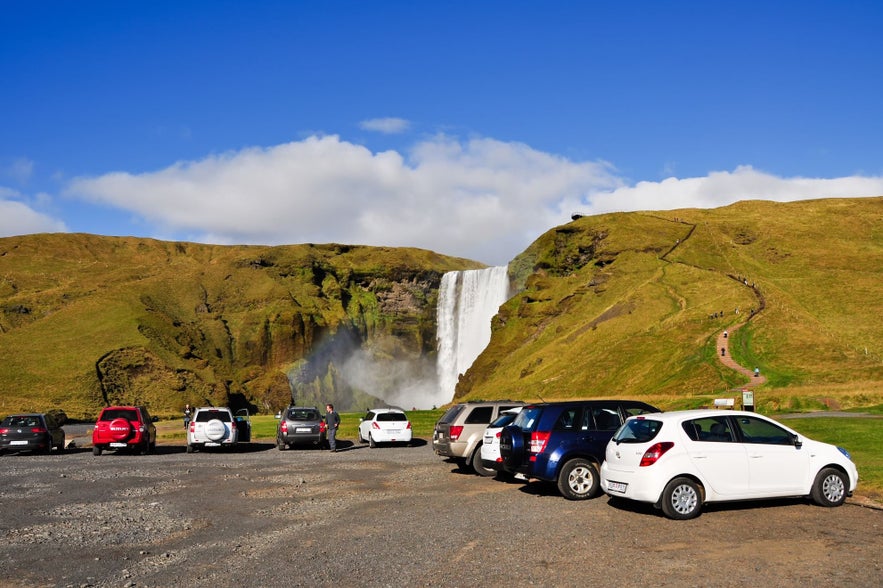 Cars are parked near Skogafoss waterfall in Iceland.