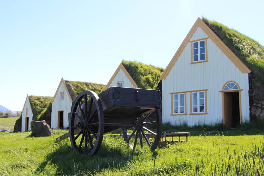 Traditional turf-roofed houses at Glaumbær Farm Museum in North Iceland on a sunny summer day, with a vintage wooden cart in the foreground. Traditional turf-roofed houses at Glaumbær Farm Museum in North Iceland on a sunny summer day, with a vintage wooden cart in the foreground.