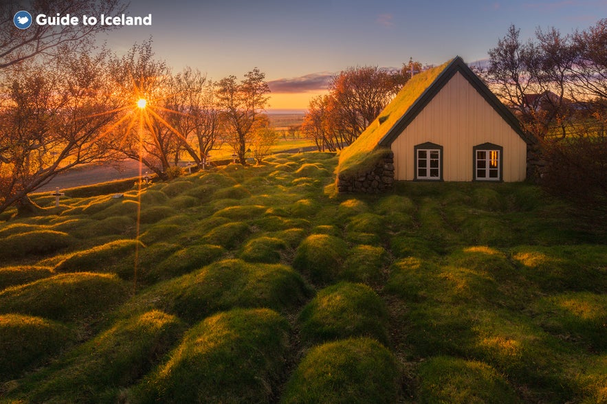 Traditional Icelandic turf church near Hof in South Iceland, bathed in golden sunset light with moss-covered graves in the foreground.
