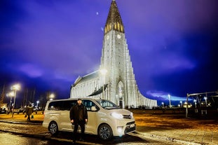 The professional driver poses with his comfortable vehicle near the beautiful Hallgrimskirkja church.