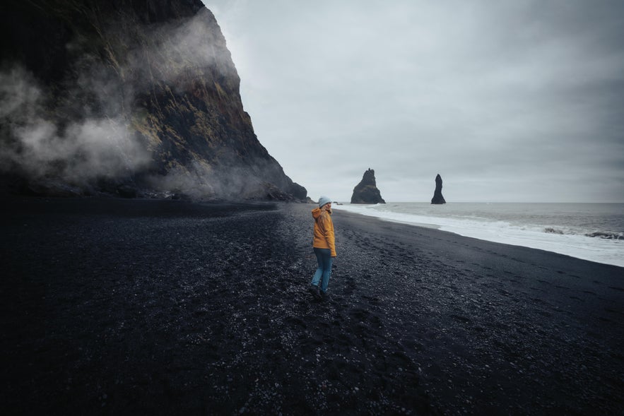 Een vrouw staat op het zwarte zandstrand van Reynisfjara.