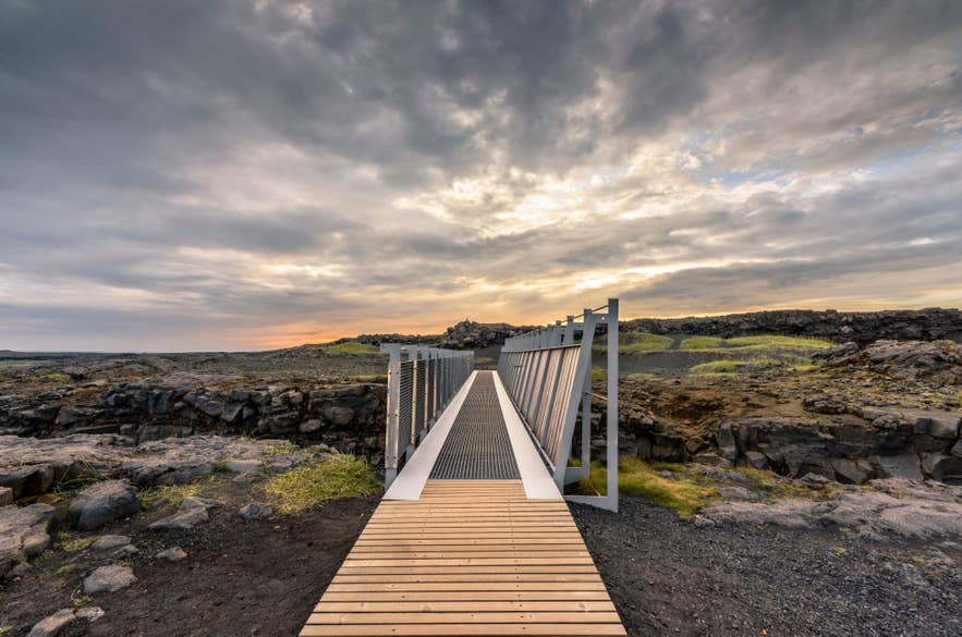 De Brug tussen de Continenten op het schiereiland Reykjanes in IJsland bij zonsondergang, als symbool voor de scheiding tussen de Noord-Amerikaanse en Euraziatische tektonische platen, omringd door ruig vulkanisch terrein.