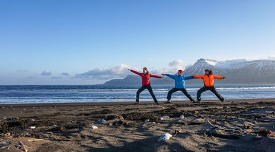 Three people stretch out their arms in warrior pose during a yoga tour in Iceland.