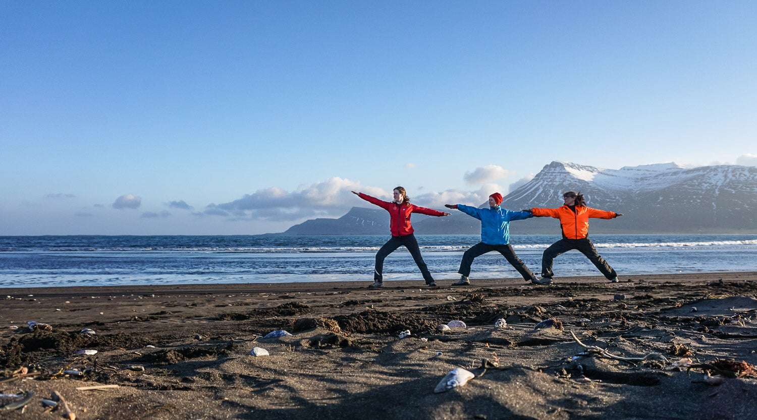 Three people stretch out their arms in warrior pose during a yoga tour in Iceland.