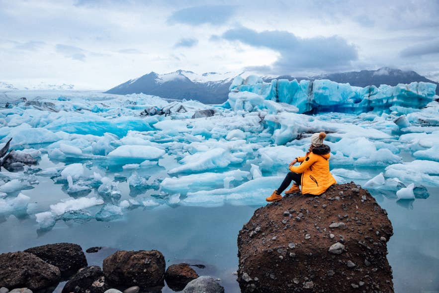 Une femme est assise sur un rocher et admire le lagon glaciaire.