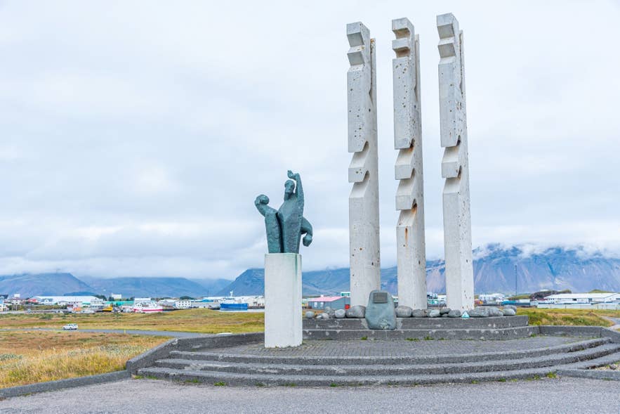 Offentlig skulptur i Höfn i Island med moderne kunstnerisk design og byen samt havnen i baggrunden.