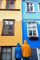 Two people wearing bright raincoats look up at two colorful buildings in Reykjavik.