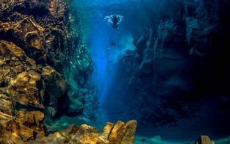 Grupa snorkelujących przemierzająca wąski błękitny kanion szczeliny Silfra w promieniach przenikającego światła słonecznego.