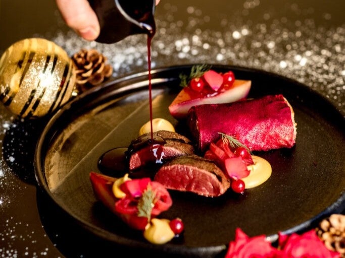 Gourmet holiday dinner at Kol restaurant in Reykjavik, featuring seared meat medallions, vibrant root vegetables, and rich sauce on a black plate with festive decor.
