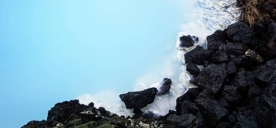 Close-up van het levendige blauwe geothermische water van de Blue Lagoon, dat contrasteert met donkere vulkanische lavastenen en witte kiezelafzettingen in IJsland.