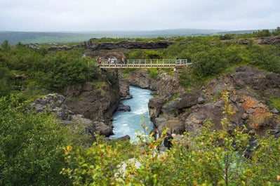 Hraunfossar falls in West Iceland flows from volcanic rock, with snow-dusted vegetation above, creating a magical landscape.