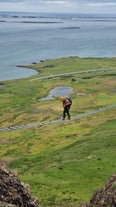 A person walking along a rope bridge above the Icelandic countryside.