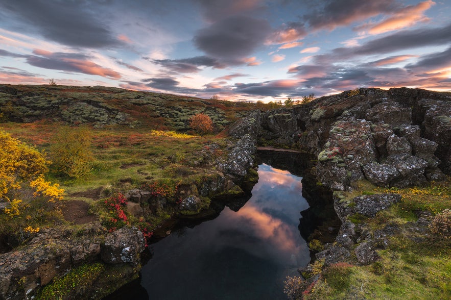 Peningagja Ravine in Thingvellir National Park, Iceland, with clear spring water and mossy lava rocks at sunset.
