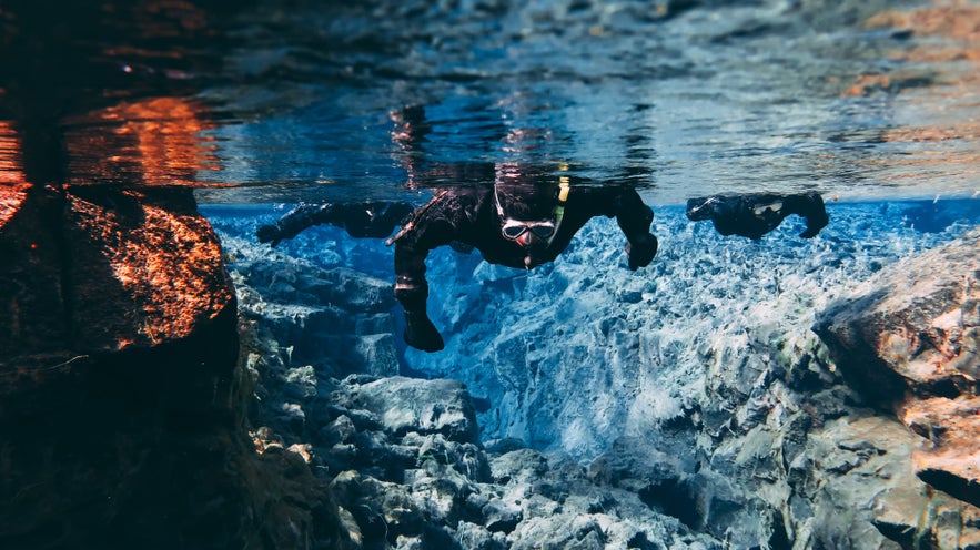 People Snorkeling swimming diving in the blue cold glacier water in famous fissure Silfra between two tectonic plates in the national park Thingvellir in Iceland. Blue transparent water, deep colors.