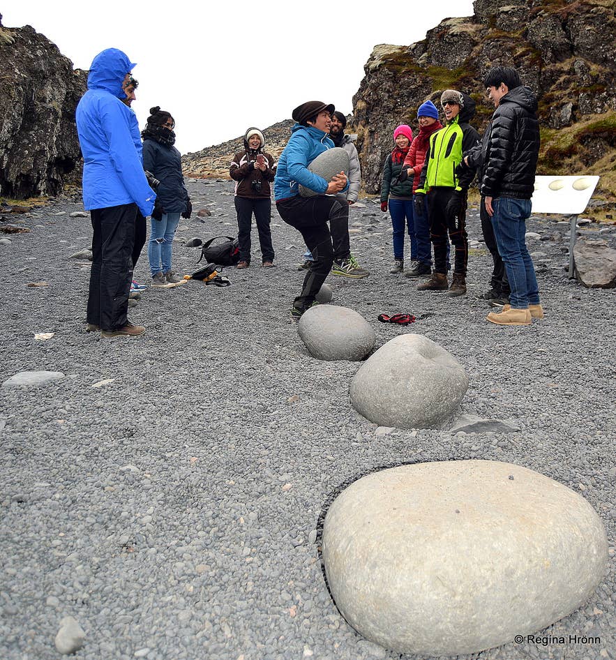 Travelers testing the lifting stones at Djupalonssandur Beach near Snaefellsjokull.