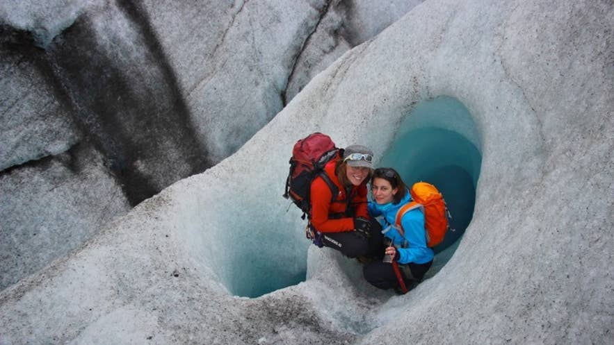 Zwei Reisende mit Rucksäcken erkunden blaue Eisformationen auf dem Skaftafell-Gletscher im Vatnajökull-Nationalpark in Island.