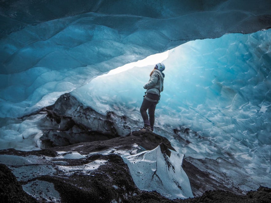 Traveler exploring a blue ice cave inside Solheimajokull Glacier, an outlet of Myrdalsjokull in South Iceland.