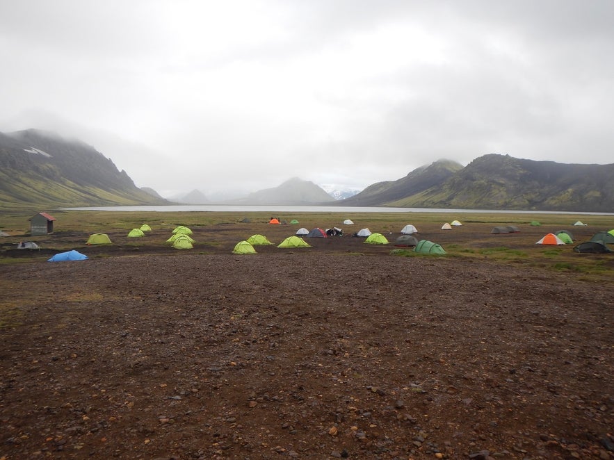 Colorful tents set up in a remote, misty highland campsite surrounded by mountains in Iceland in July.