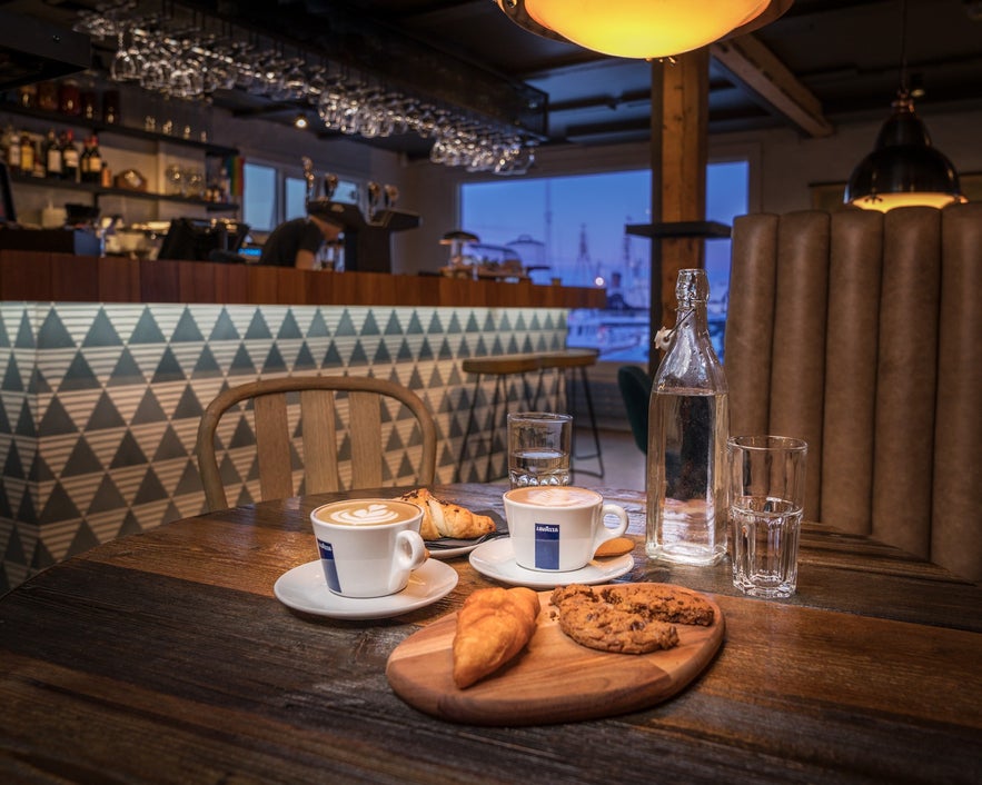 Cozy waterfront view from inside Reykjavik Röst café with coffee cups and harbor backdrop.