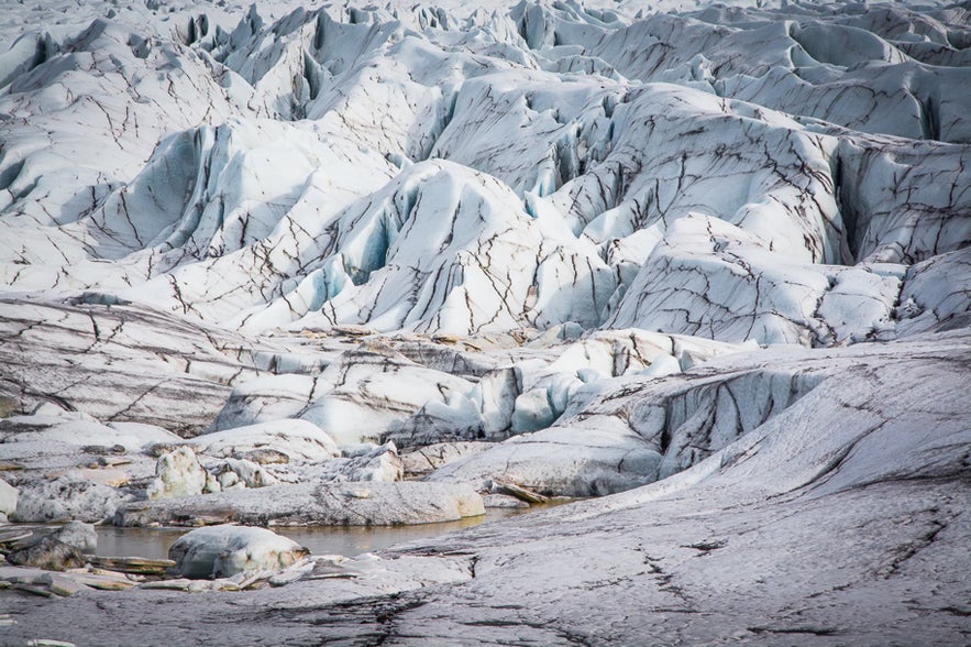 The movement of glaciers creates tensile strain on their brittle upper sections, causing them to break and create crevasses.