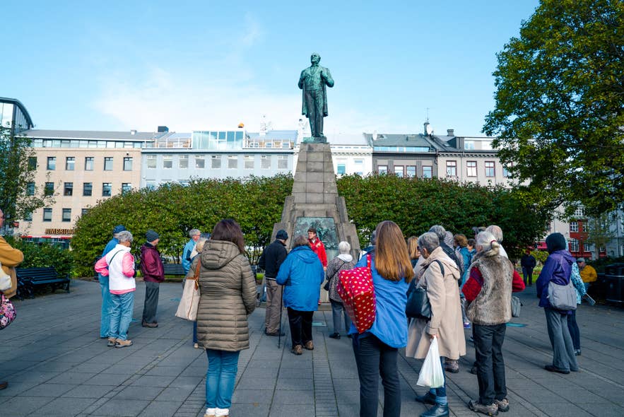 A walking tour group gathered around the Jón Sigurðsson statue on Austurvöllur square.