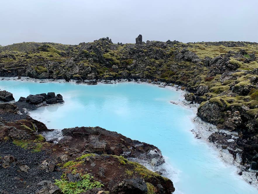 Bright blue geothermal pool surrounded by moss-covered lava rocks in the Blue Lagoon area of Iceland, under overcast skies. Bright blue geothermal pool surrounded by moss-covered lava rocks in the Blue Lagoon area of Iceland, under overcast skies.
