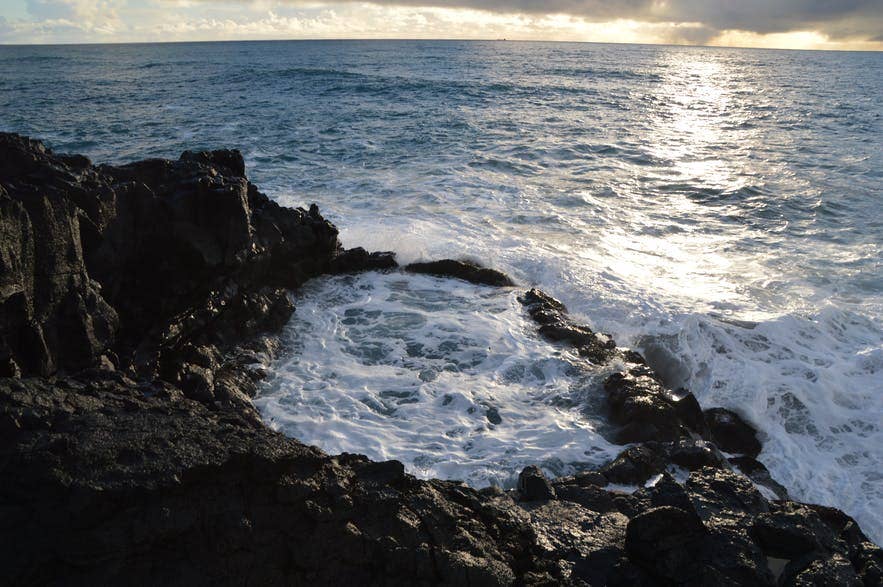 Brimketill lava rock pool on the Reykjanes Peninsula, Iceland, with ocean waves crashing against the rugged volcanic coastline at sunset.