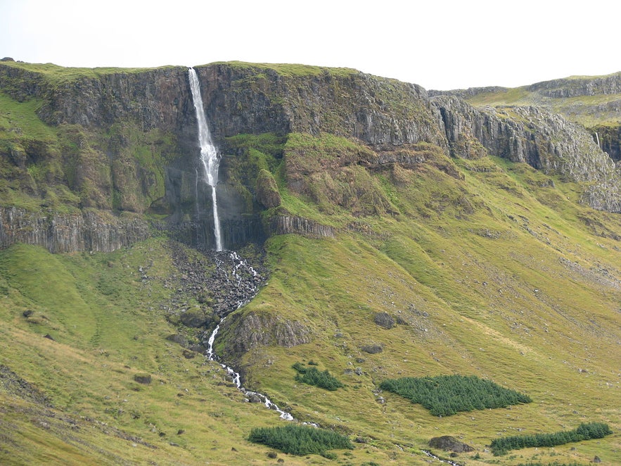 Bjarnarfoss waterfall on the Snaefellsnes Peninsula in West Iceland, cascading from a high cliff into a green mountainside with scenic views.