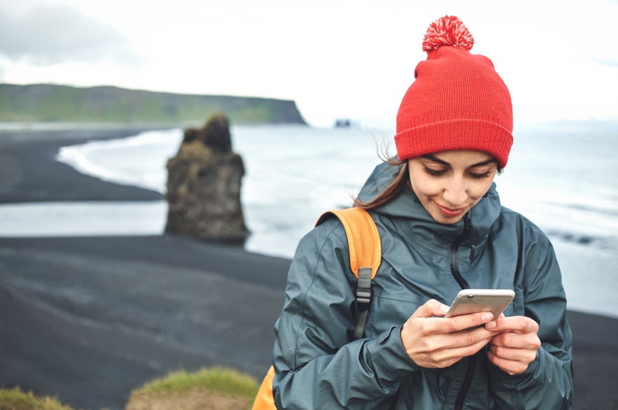 A woman looks at her phone by Reynisfjara.