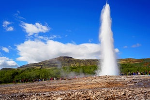 A group of travelers marveling at the dramatic water eruption of Strokkur in the Golden Circle.