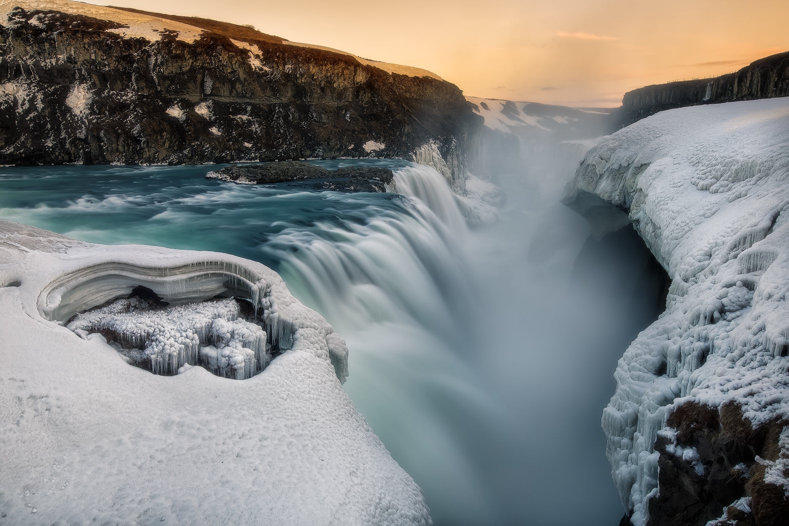 La cascada Gullfoss fluye entre acantilados helados al atardecer durante el invierno a lo largo de la ruta del Círculo Dorado en Islandia.