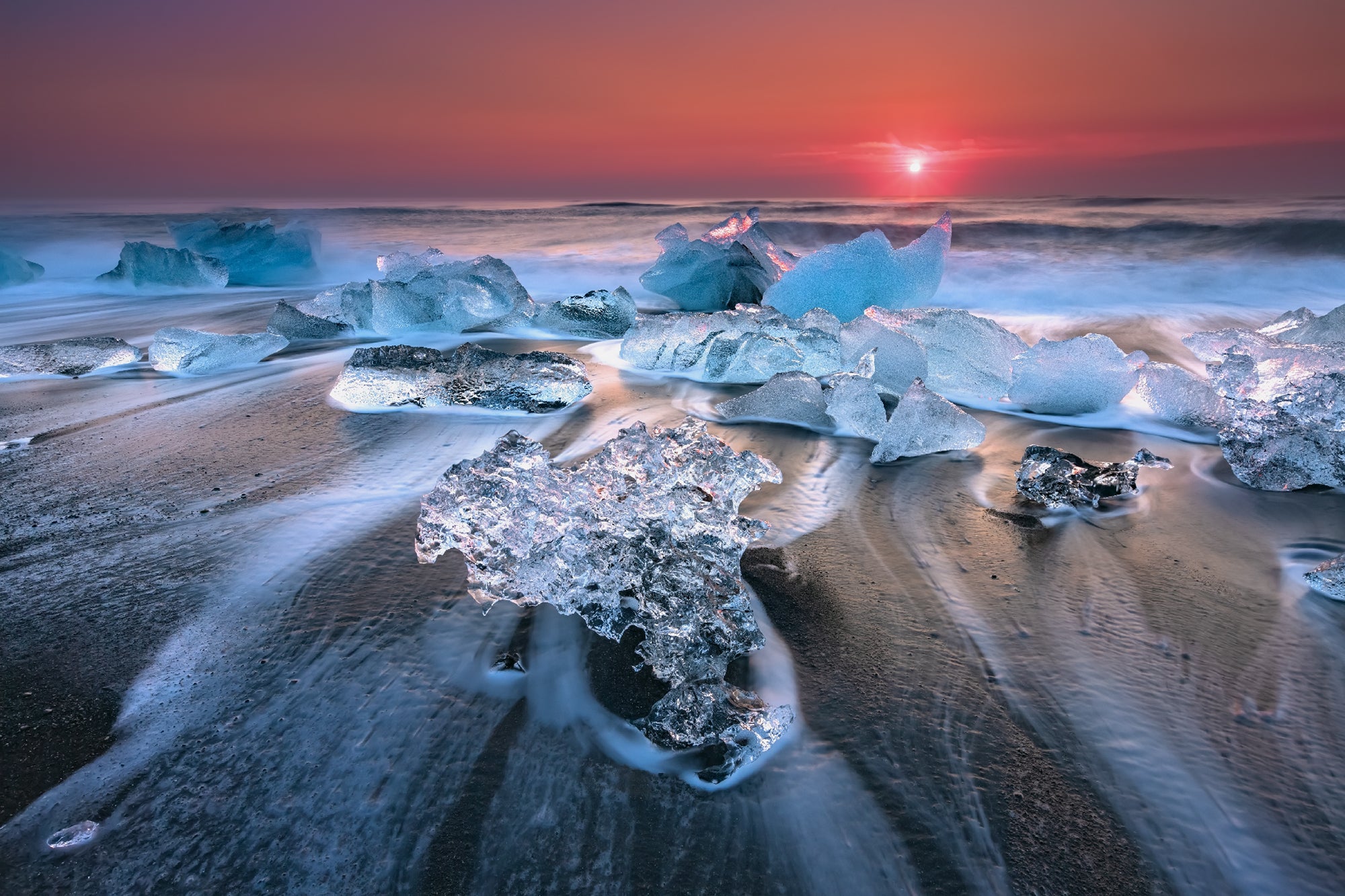 La glace du glacier brille sur le sable noir de la Plage de diamants en Islande au lever du soleil, créant une scène côtière magique.