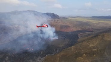Een rode helikopter zweeft boven een dampend lavaveld bij de vulkaan Fagradalsfjall op het schiereiland Reykjanes.