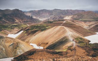 Hikers traverse a narrow trail along the spine of a red slope in Landmannalaugar, reachable via a bus transfer from Reykjavik.