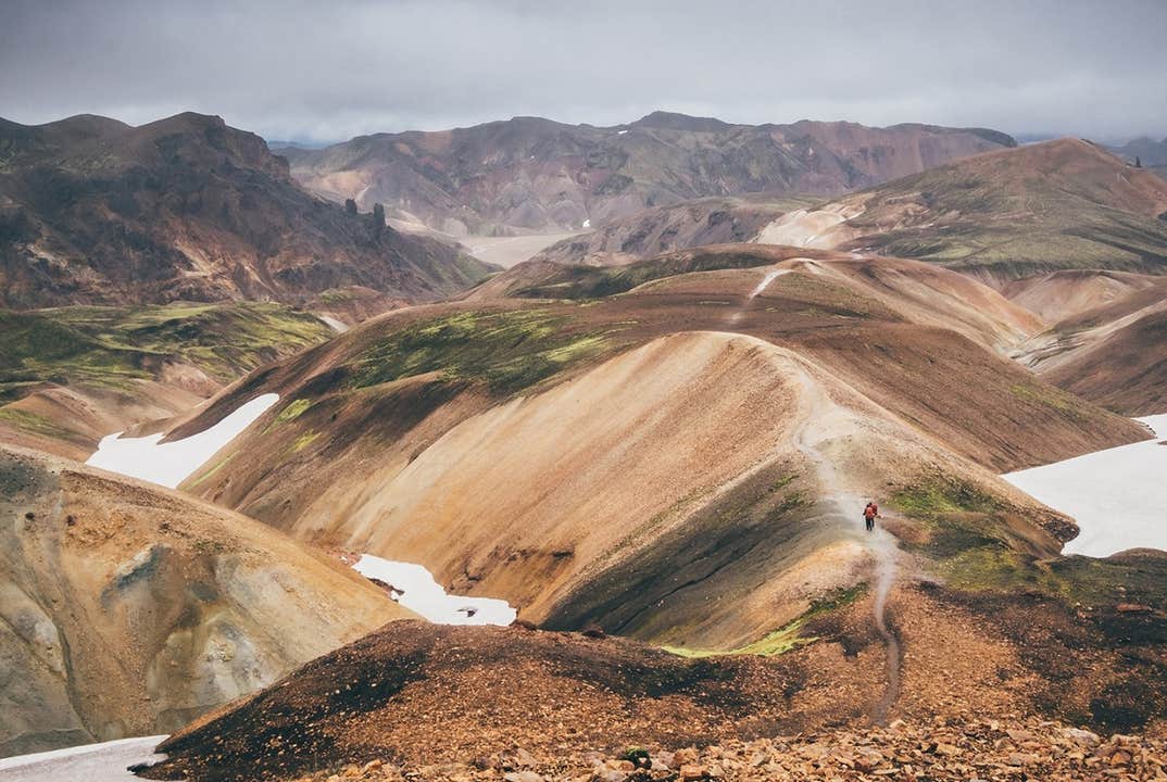 Vandrere følger en smal sti langs ryggen af en rød skråning i Landmannalaugar, som kan nås med bus fra Reykjavik.